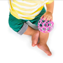 Baby holding a pink ball rattle with an open lattice grip and colorful beads