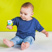 Plush wrist rattle teether on baby hand with white-and-blue animal face and green strap