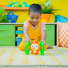 Monkey baby roll-and-glow toy with orange face and green loop handles, light-up rings