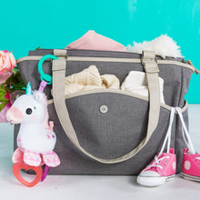 Unicorn plush clip-on toy attached to a gray tote bag with teal ring handle