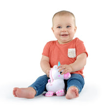 Unicorn plush clip-on toy held by a baby; teal handle, pink snout, patterned legs
