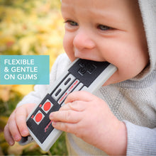 Baby biting a grey controller-shaped silicone teether with red button details