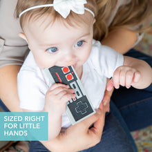 Controller-shaped silicone teether held by a baby, grey with red button details