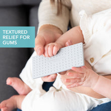 Silicone teether with textured bumps, held by a baby in white clothing