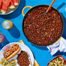 Baked beans serving bowl with hot dog and plates of beans on table