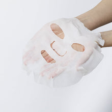 Sheet face mask held in hand, translucent white with beige areas