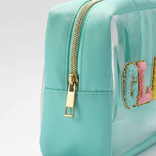 Teal cosmetic bag close-up with gold zipper pull and glitter “GLAM” logo