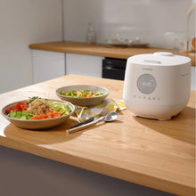 White CUCKOO 6-cup rice cooker on kitchen counter beside bowls of food