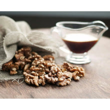 Walnuts scattered on a wooden board with a small glass bowl of dark liquid