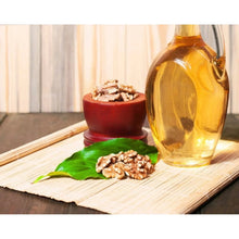 Walnuts in a red bowl with a glass bottle of oil on a wooden board