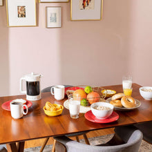 Coffee and breakfast table with mugs, kettle, fruit, and pastries