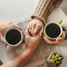 People holding coffee mugs above an open bag of coffee beans