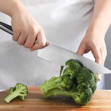 Chef knife cutting broccoli on a wooden board, hands holding a stainless blade