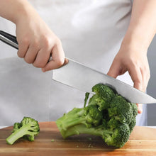 Chef knife with dark handle and silver blade, slicing broccoli during food prep