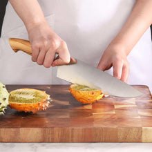 Hands cutting food with a stainless steel knife on a wooden cutting board