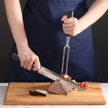 Carving knife and fork with dark handles over sliced meat on wooden board