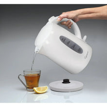 White electric water kettle pouring water into a glass cup, with lid open