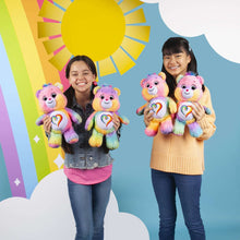 Four Togetherness Bear plushes with rainbow heart bellies held by two kids.