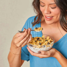 Bowl of blueberry muffin cereal with milk, blueberries mixed in, held by a person.