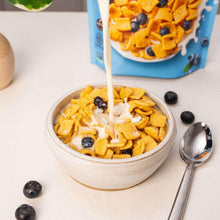 Bowl of blueberry muffin cereal with milk and blueberries on top, spoon beside bowl.
