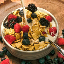 Bowl of cereal flakes topped with mixed berries and a spoon