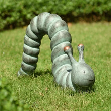 Garden caterpillar statue on grass, curled body with antennae and copper-tipped details