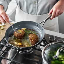 Ceramic nonstick skillet cooking steaks in skillet with oil and herbs