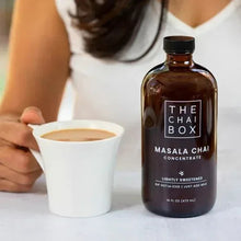 Chai concentrate bottle beside a white cup with hands preparing to pour