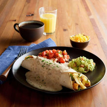 Sausage with white country gravy served on a plate with vegetables and roll.