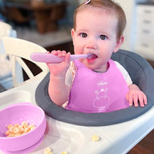 Pink silicone baby bib with bunny graphic while holding a pink feeding spoon
