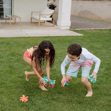 Reusable sponge balls in children’s hands with colorful foam pieces on lawn.