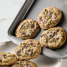 Grey baking sheet filled with baked cookies topped with nuts and herbs