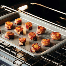 Grey nonstick baking tray with sliced rolls baking in an oven