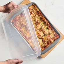 Grey nonstick loaf pan with a clear lid held over a wooden board