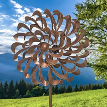 Metal pinwheel wind spinner with brown pinwheel blades on tall pole against open sky.