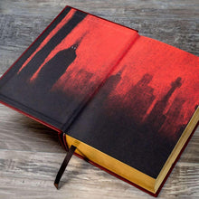 Hardcover horror book, open to red and black artwork pages with a ribbon bookmark