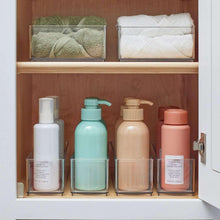 Clear shelf organizer bins with folded towels and assorted bottles