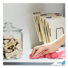 Hand wiping countertop with pink microfiber cloth near jars and storage binders