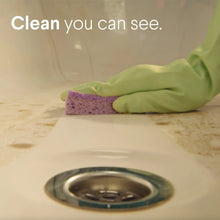 Gloved hand wiping a countertop with a sponge near a metal sink drain