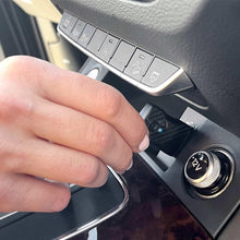 Wireless car adapter being plugged into car USB port; carbon-fiber casing visible