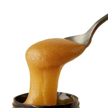 Manuka honey pouring from a spoon, thick golden amber stream.