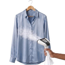 Hand steams a light blue button-up shirt with handheld steamer near chest area