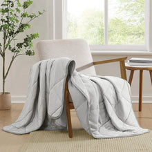 Light gray quilted cooling throw blanket with draped fold over chair