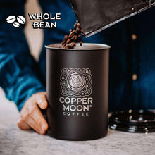 Copper Moon whole bean coffee bag pouring beans into black coffee mug