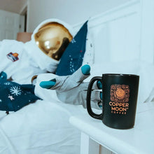 Black Copper Moon coffee mug on a bedside table with a person in the background