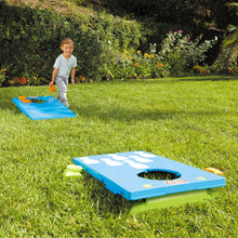 Blue cornhole game board with green base on grass, with orange bean bag