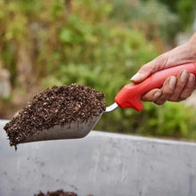Red-handled hand shovel scooping soil from a garden bed