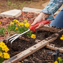 Red-handled digging tool loosening soil around small flowers in a garden bed