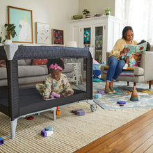 Portable baby play yard set up on floor with mesh sides and padded interior