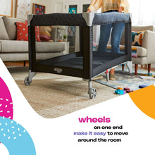 Dark mesh baby play yard with wheels, standing indoors on a carpeted floor